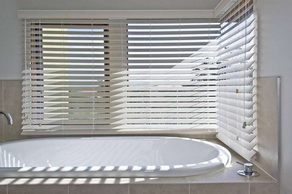 A bathroom & bathtub with sunlight shining through the shuttered windows | Featured image for the Indoor Privacy Blinds Page on Shutters Blinds & Awnings.